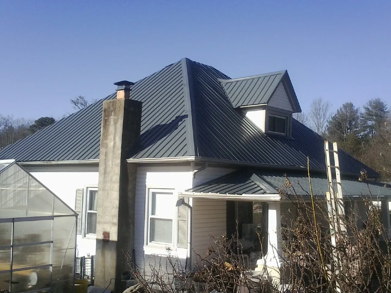 Dark blue standing seam metal roof on a white farmhouse with dormer — Slate & Tile Roof Repair by Roofing Brothers in Northborough