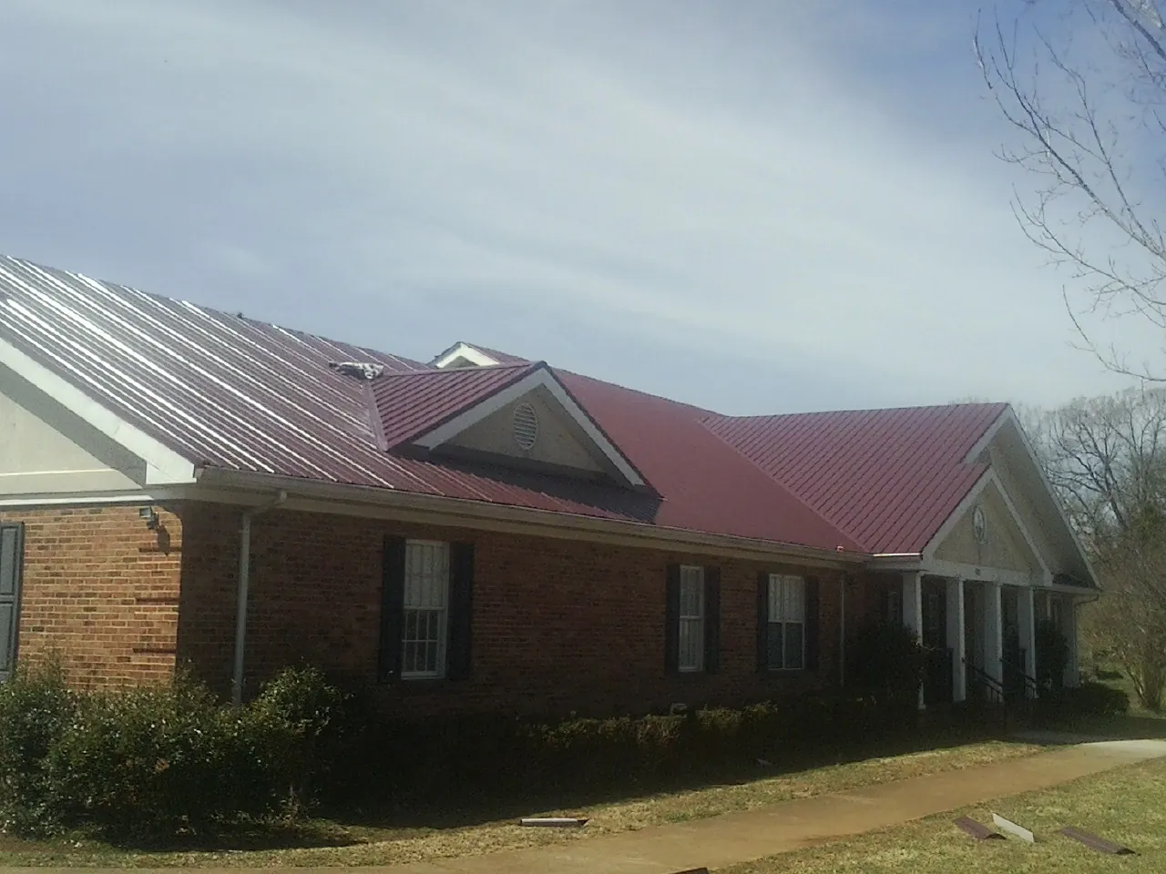 Red metal roof with gabled entries on a long brick building, from a Hail Damage Roof Repair job in Northborough