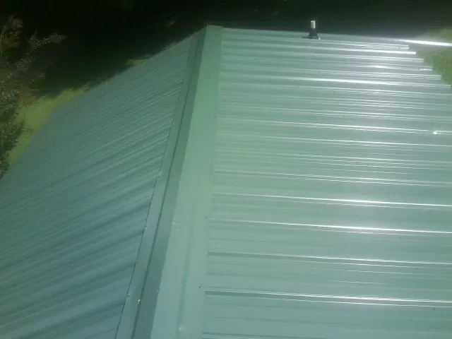 New green metal panels meeting at the ridge of a roof — Flat Roof Repair work by our crew in Northborough