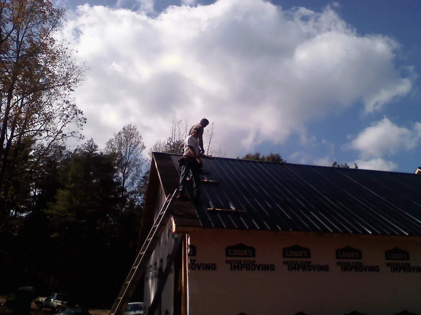 Roofer fastening dark metal panels high against a cloudy sky, from a Roof Inspection job in Northborough