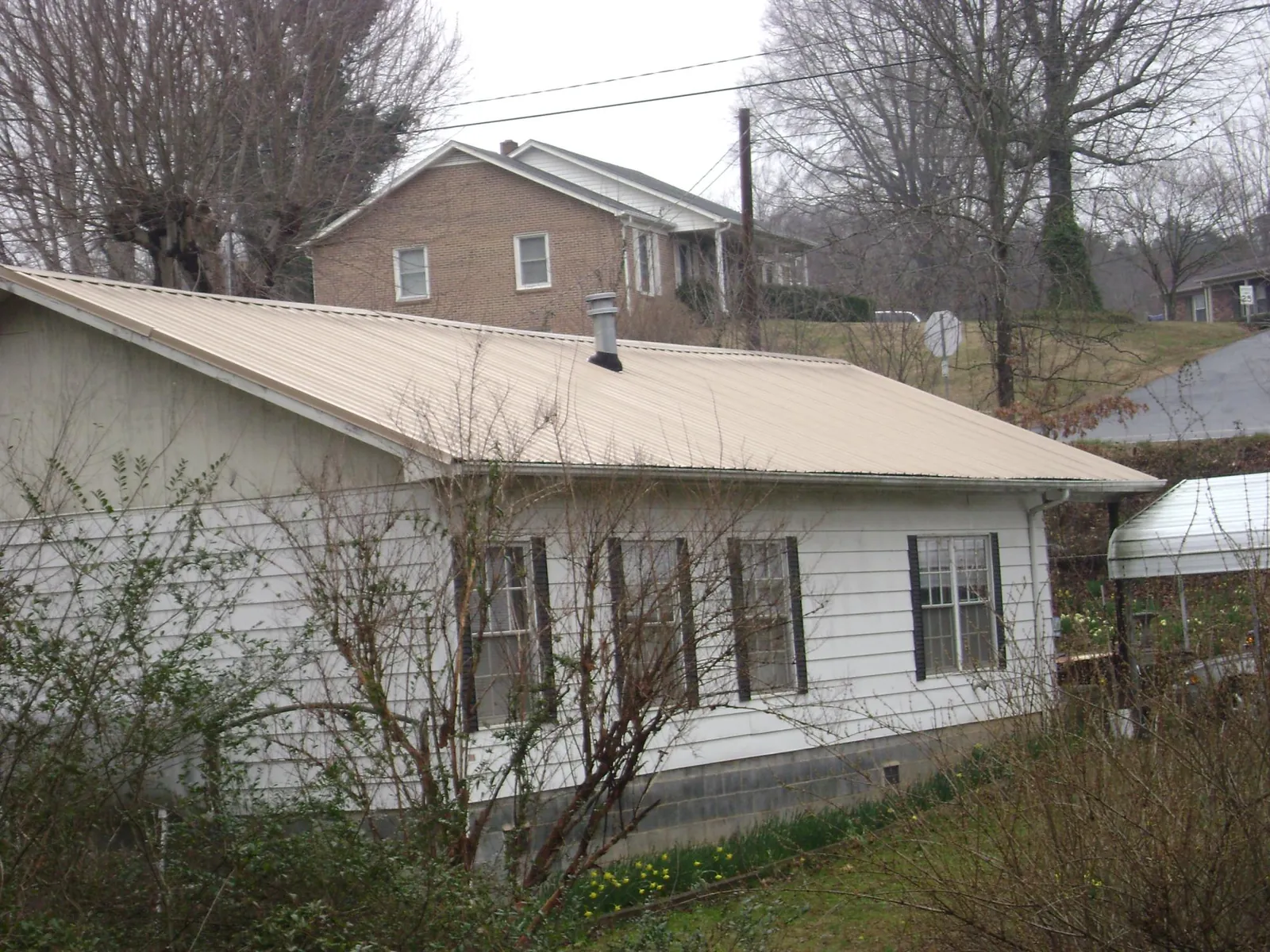 Tan metal roof on a white sided house set into a hillside — Commercial Roofing by Roofing Brothers in Northborough